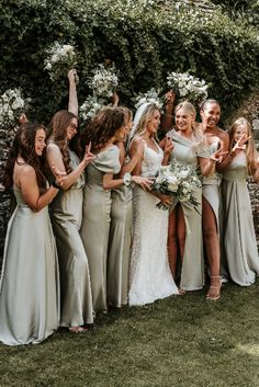 a group of women standing next to each other in front of a stone wall holding bouquets