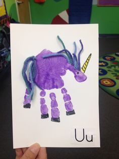 a child's hand holding up a purple animal made out of paper with the letter u on it