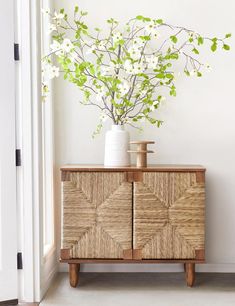 a vase with white flowers in it sitting on top of a wooden cabinet next to a wall