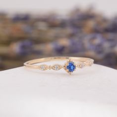 a blue and white diamond ring sitting on top of a stone slab with lavender flowers in the background