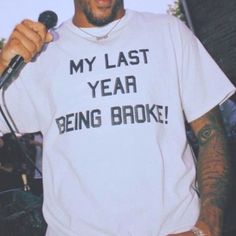 a man holding a microphone and wearing a t - shirt that says my last year being broke