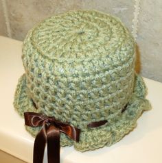 a green crocheted hat with a brown ribbon around the brim and bow