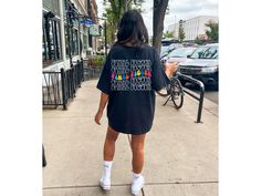 a woman is walking down the sidewalk wearing a black t - shirt with rainbows on it