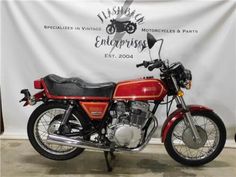 a red and black motorcycle parked in front of a white wall with a sign behind it