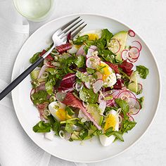 a white plate topped with a salad next to a glass of milk and a fork