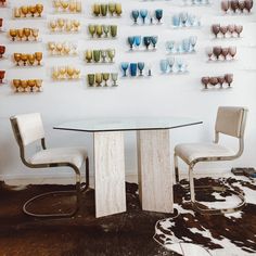 two chairs and a table in front of a wall with wine glasses on the wall