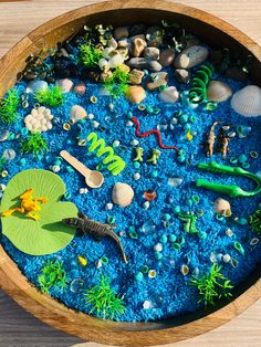 a wooden bowl filled with lots of different types of toys and sea life on top of blue sand