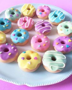 a white plate topped with lots of colorful donuts on top of a pink table