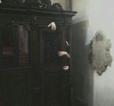 a person reaching out from behind a wooden cabinet in a room with a mirror on the wall