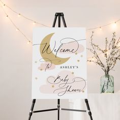 a welcome sign is on an easel next to a vase with flowers and lights