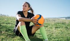 a woman sitting in the grass holding an orange ball with her hands on her knees