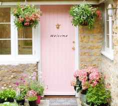 a pink door with welcome written on it and potted flowers in the foreground