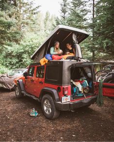 two women sitting in the back of a red jeep with an awning on it