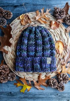 a knitted hat sitting on top of a basket filled with leaves and pine cones