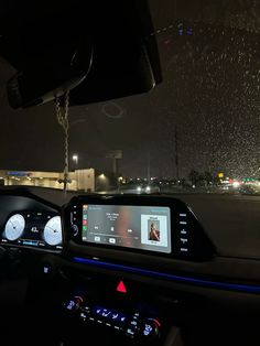 the dashboard of a car at night with rain falling on it and buildings in the background