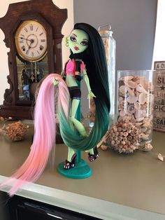 a doll with long hair sitting on top of a counter next to an old clock