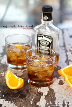 two glasses filled with ice and orange peels next to an old fashioned liquor bottle