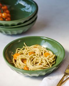 two green bowls filled with pasta and garnished with oranges on the side