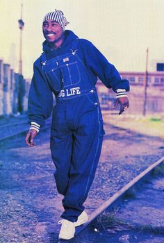 a man in blue jumpsuits standing on train tracks with his arms out to the side