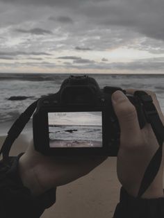 a person holding up a camera to take a photo with the ocean in the background