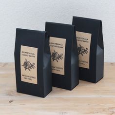 three black boxes with labels on them sitting on a wooden table next to a white wall