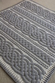 a gray and white knitted area rug on the floor with an intricate design in the middle