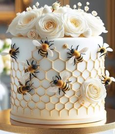 a bee themed cake with white roses and bees on the top is sitting on a table