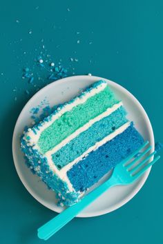 a piece of blue and green cake on a plate next to a fork with sprinkles