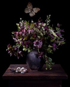 a vase filled with purple flowers and butterflies on top of a wooden table in front of a black background