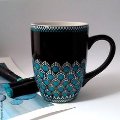 a black and blue coffee cup sitting on top of a table next to a pen