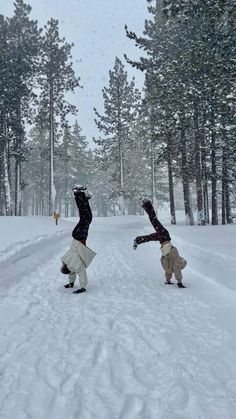 two people doing tricks in the snow near trees