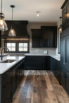 a large kitchen with black cabinets and white counter tops, wood flooring and pendant lights