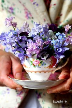 a person holding a tea cup with purple flowers in it and wearing a white dress