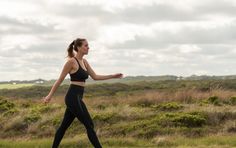 a woman is running in the grass on a cloudy day