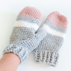 a pair of crocheted mittens sitting on top of a white table next to a person's hand