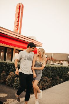 a man and woman are walking down the sidewalk in front of a building with a neon sign