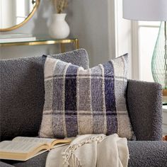 a gray couch with a book on it and a mirror in the corner behind it