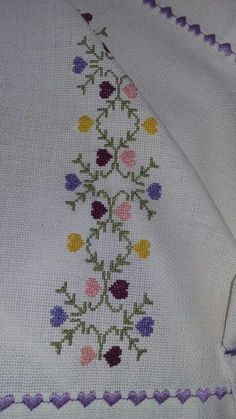 a cross - stitched blanket with flowers on it and purple trim around the edges