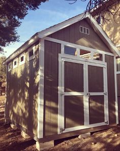 a small shed sitting on top of a dirt field next to a building with windows