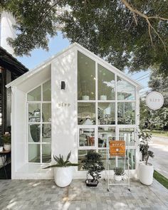 a small white house sitting on top of a brick floor next to a lush green forest