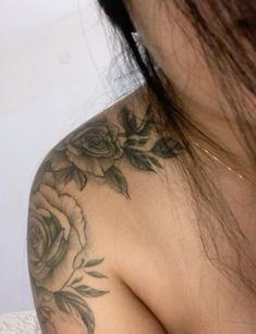 a close up of a woman's shoulder with tattoos on it and flowers in the back