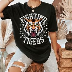 The Fighting Tigers t-shirt is perfect for all the sporting events. This retro and funky tiger tee is everything you've dreamed of and more. This adorable and soft shirt makes a great gift for tiger fans to wear to all the sporting events or just everyday wear! It feels soft and lightweight, with the right amount of stretch. It's comfortable and flattering for all.  Show off your personality with our fun and unique designs!   ** P R O D U C T   D E T A I L S **  - High Quality, Super Soft and Co Sports Fan Graphic Print T-shirt For College, Black Sports Fan Top With Graphic Print, Collegiate Graphic Print Shirt For Sports Events, Black Tops With Graphic Print For School Spirit, Graphic Print T-shirt For Sports Events, Black School Spirit Tops With Graphic Print, Black School Spirit Graphic Tops, Graphic T-shirt For Sports Events, Short Sleeve Graphic Print Shirt For Sports Season