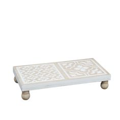 a white coffee table with an intricate design on the top and two small wooden legs