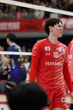 a man in red jersey standing next to a volleyball ball on a court with people watching