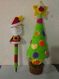 a green christmas tree next to a pencil holder with a santa clause figure on it