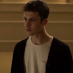 the young man is standing in front of some stairs wearing a white t - shirt and black cardigan