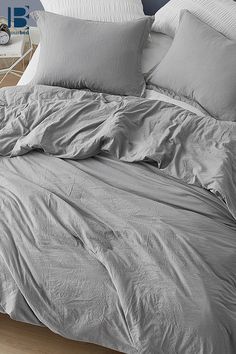 an unmade bed with grey sheets and pillows