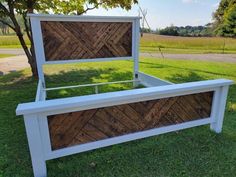 a bed frame made out of wood and white paint on the grass with trees in the background