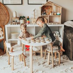 two young children playing with cups and plates in a play room filled with furniture, toys and decor