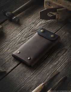 a leather wallet sitting on top of a wooden table next to hammers and other tools